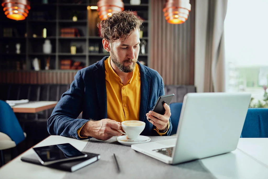 Un homme qui bois un café devant son ordinateur portable dans un café pour travailler en freelance par internet